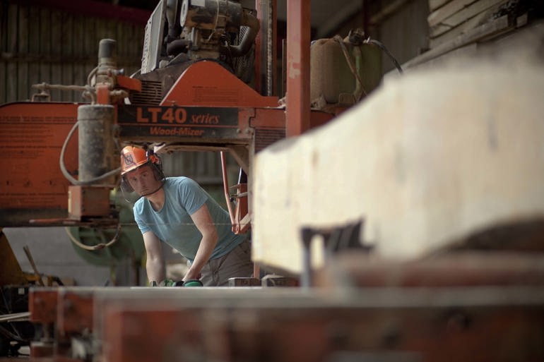 Man working in a saw mill cutting large piece of timber Man working in a saw mill cutting large piece of timber