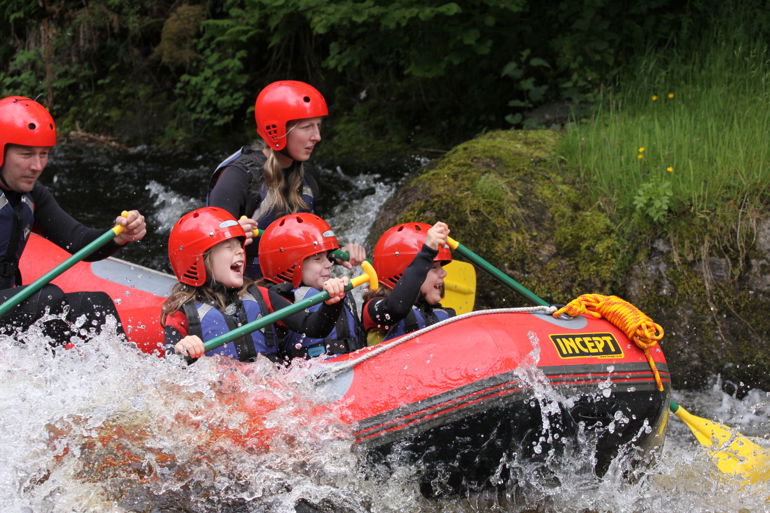 Children and adults paddling in a boat down rapids Children and adults paddling in a boat down rapids