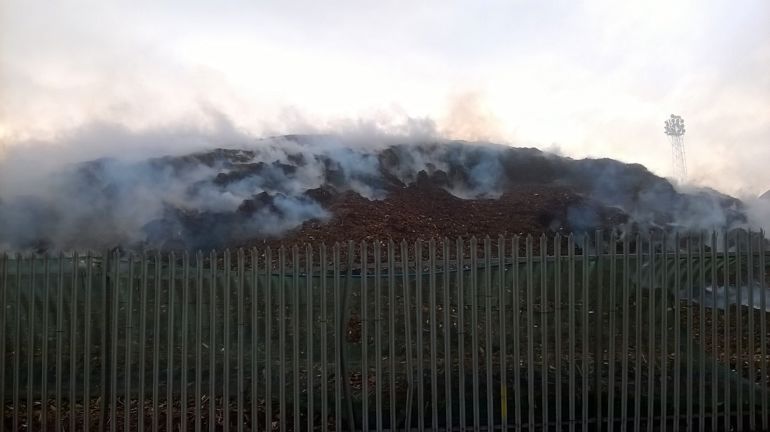 Smoke bellowing from a pile of wood chip surrounded by a metal fence Smoke bellowing from a pile of wood chip surrounded by a metal fence