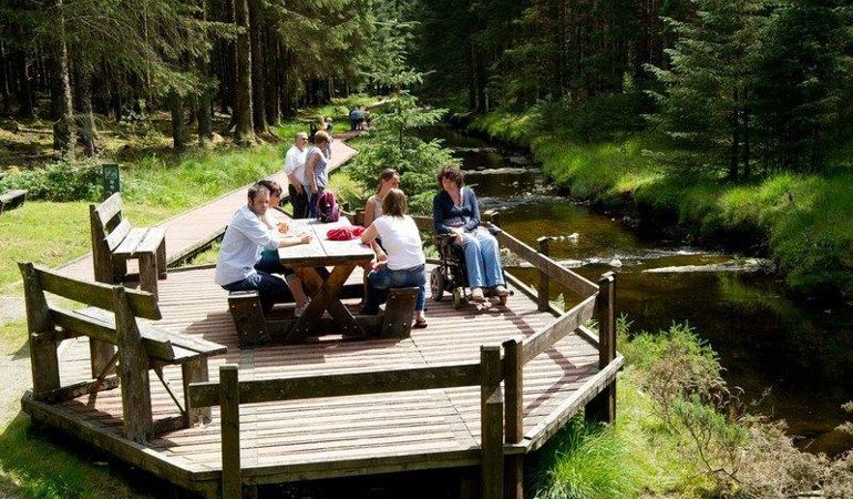 People gathered around a picnic bench next to a river. People gathered around a picnic bench next to a river.