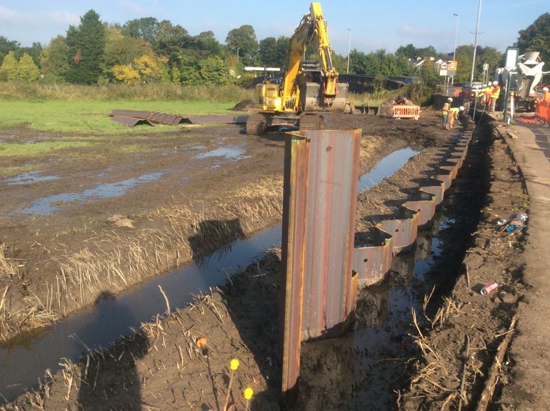 Digger in a muddy field building a steal flood defence Digger in a muddy field building a steal flood defence