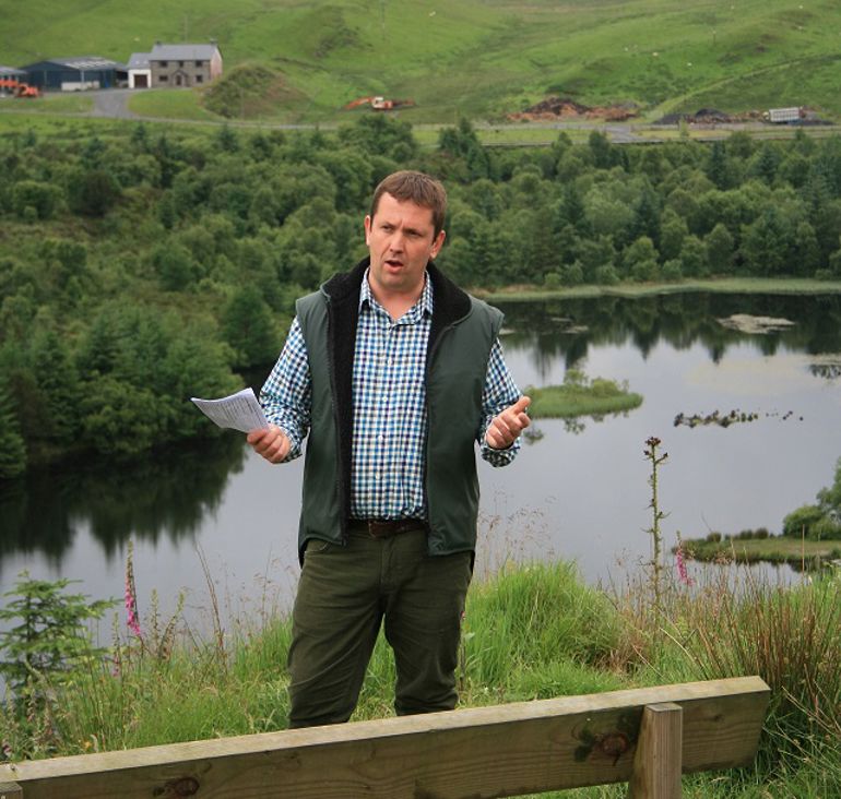 Man in checked shirt and waistcoat stood at the side of a lake with piece of paper in his hand Man in checked shirt and waistcoat stood at the side of a lake with piece of paper in his hand