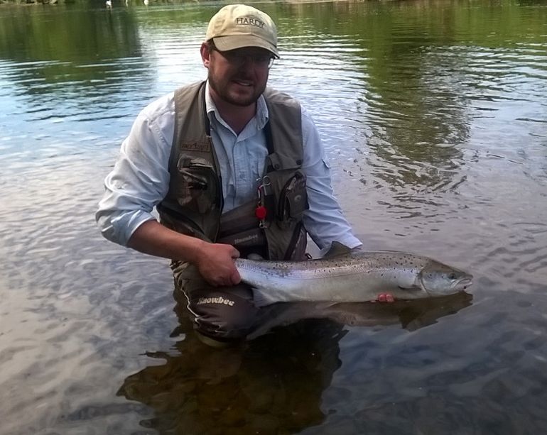 Angler holding a salmon while standing in the River Usk Angler holding a salmon while standing in the River Usk