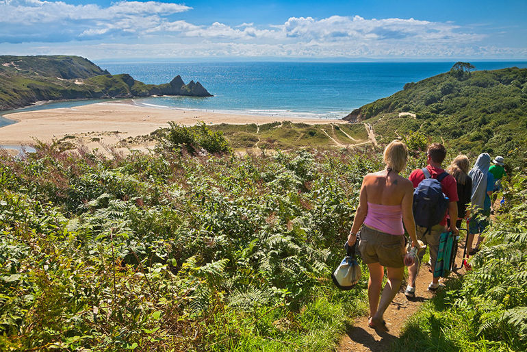 Group of people walking towards the beach at 3 Cliffs Bay Gower Group of people walking towards the beach at 3 Cliffs Bay Gower