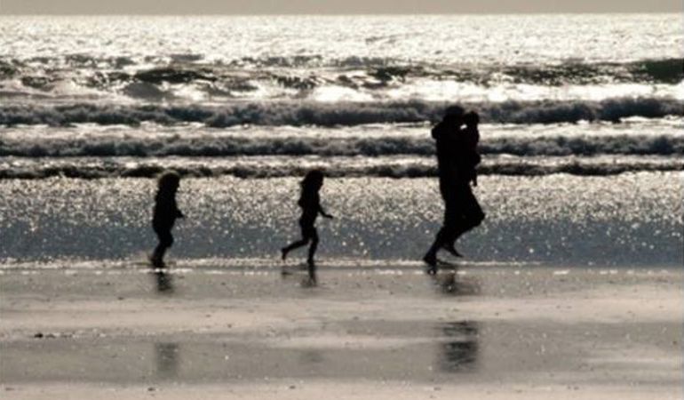 Llun o deulu yn rhedeg ar draeth ger y môr Llun o deulu yn rhedeg ar draeth ger y môr